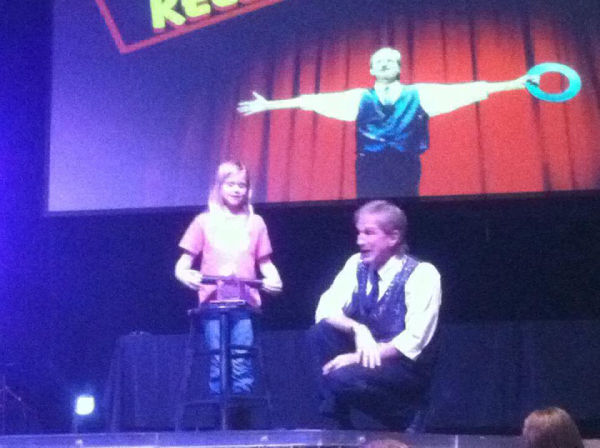 Rodney the Magician on stage interviewing a girl volunteer